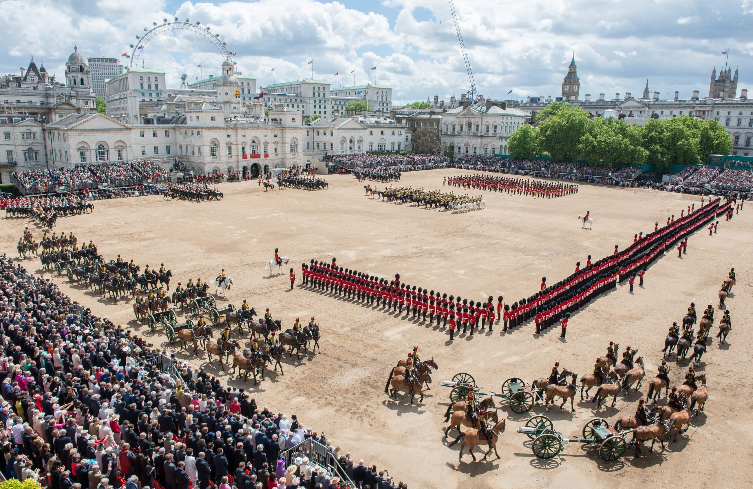 Massed ranks of the Household Division in red tunics and bearskin caps on Horse Guards Parade during Trooping the Colour in London, mounted officers in front of the lines.