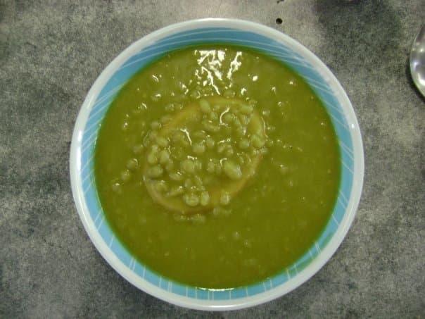 A pie floater: a meat pie sunk in a bowl of thick green pea soup on a blue-rimmed plate.